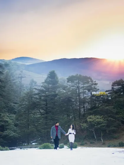 A stunning sunset shot of a couple walking in a snow-covered landscape, with the golden sun creating a beautiful flare over the mountains.