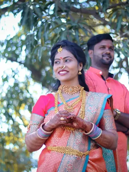 A lovely portrait of a bride and groom in their wedding attire, standing together outdoors. The bride is in the foreground, with the groom smiling just behind her.