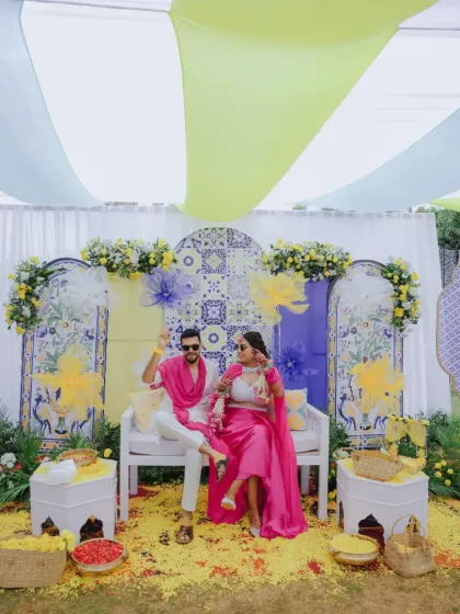 A beautiful Haldi setup inspired by Mediterranean aesthetics, using blue and yellow tiles as a backdrop. The light fabric drapes and floral arrangements create a fresh, summery feel.