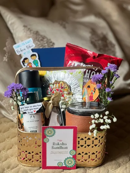 A premium Rakhi hamper for a brother, featuring a leather-wrapped tumbler, shower gel, and snacks in a decorative gold basket.