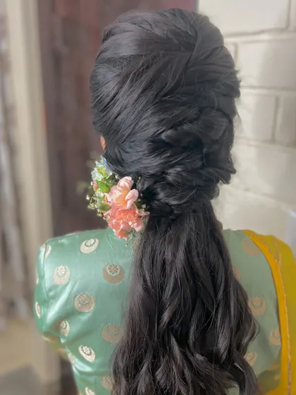 A complex and voluminous braided ponytail with a floral accessory, a true statement hairstyle.