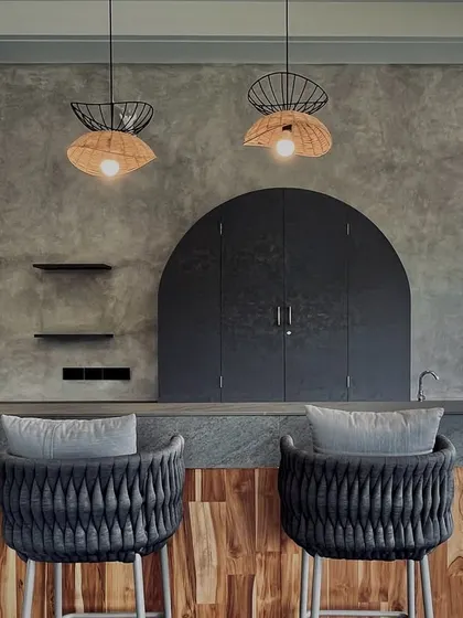 A closer view of the bar, highlighting the textures. The rough finish of the concrete wall contrasts with the warm wood paneling and the intricate weave of the bar stools, while wicker pendant lights add a natural, crafted element.
