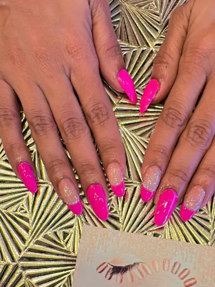 A vibrant and modern design on long, stiletto nails. This set features a sheer base with hot pink tips and a silver glitter line defining the smile line.