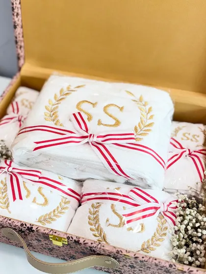A custom bride box filled with personalized towels, each embroidered with the couple's initials in a beautiful gold wreath design.