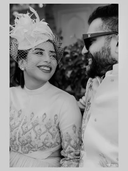 A beautiful black and white close-up of the bride, her smile radiant in a vintage-style fascinator, capturing a moment of joy at a royal-themed event.