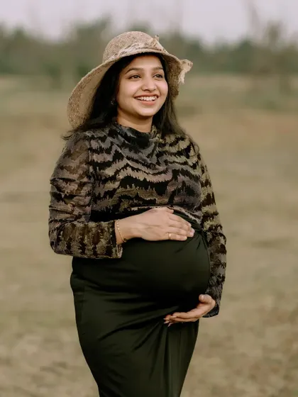 A solo maternity portrait capturing the pure happiness of a mother-to-be. Her joyful smile and the natural, open field setting create a sense of peace and contentment. The simple hat adds a touch of timeless style.