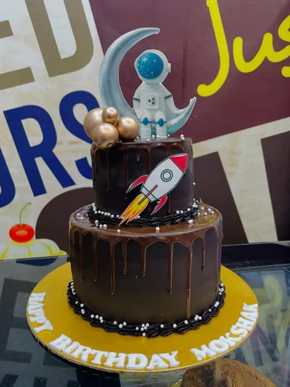 A 3.5kg two-tiered chocolate drip cake with a space theme, topped with a fondant astronaut and rocket ship.