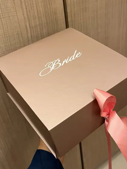 A simple yet elegant gift box for the bride. The rose gold box is customized with 'Bride' in a beautiful script and tied with a satin ribbon, ready to be filled with thoughtful goodies for her new journey.