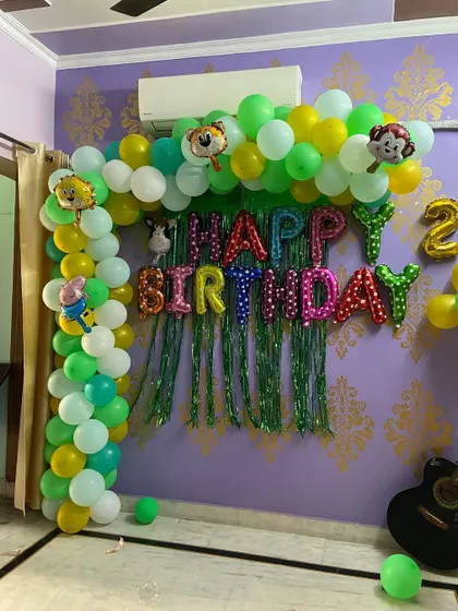 A fun jungle safari theme for a kid's birthday party at home. This setup includes a green and yellow balloon arch with animal character foils and a 'Happy Birthday' backdrop, perfect for a lively celebration.