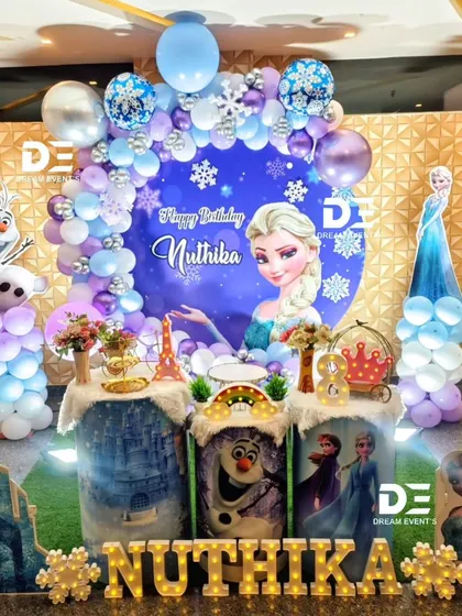 A grand 'Frozen' themed party for Nuthika's 8th birthday. The stage includes a large circular backdrop with Elsa, character cutouts, and themed pedestals depicting scenes from the movie.