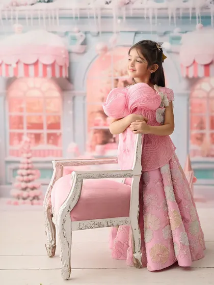 This portrait is set in a pastel-pink, candy-themed wonderland. The elaborate background and the girl's elegant pose create a stunning, high-fashion look for a children's photoshoot.
