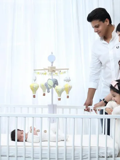 A family of four welcomes their newest member in a bright and airy lifestyle newborn session. This photo captures the whole family admiring the baby in the nursery crib.