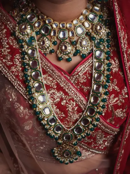 Details are the soul of a wedding's story. This close-up of the bride's kundan and emerald necklace against her embroidered red blouse highlights the exquisite craftsmanship and the care that went into choosing every element of her bridal look.