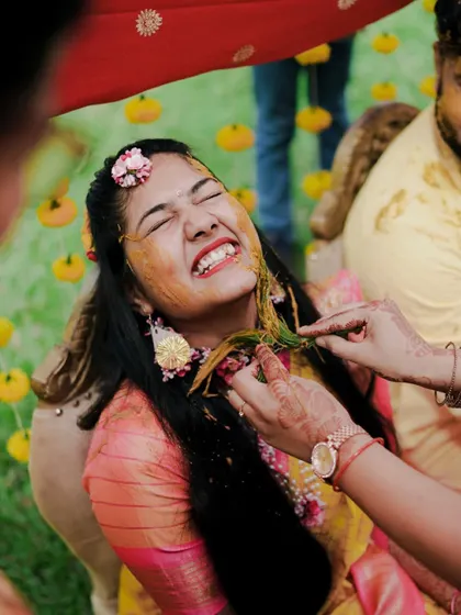 A duplicate of a close-up capturing the bride's ecstatic laugh as she gets playfully smeared with turmeric paste.