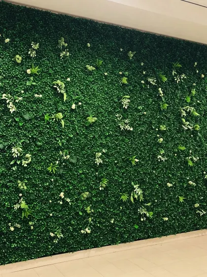 A dense and uniform artificial hedge wall, dotted with small white flowers. This type of green wall provides a clean and simple backdrop of greenery for any space.
