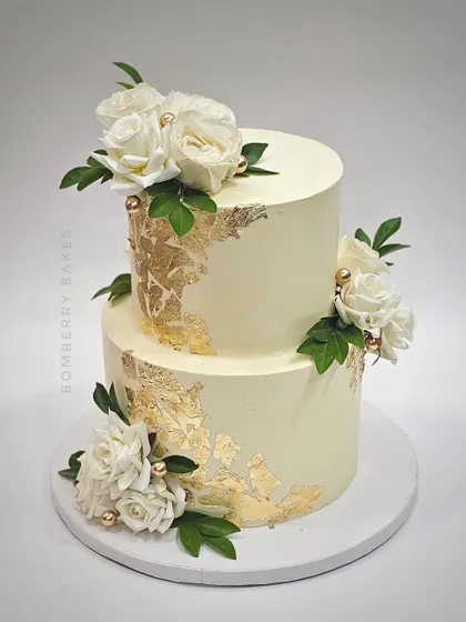 A two-tier buttercream cake with white roses and gold leaf accents. This design is perfect for a chic and modern engagement party or intimate wedding.
