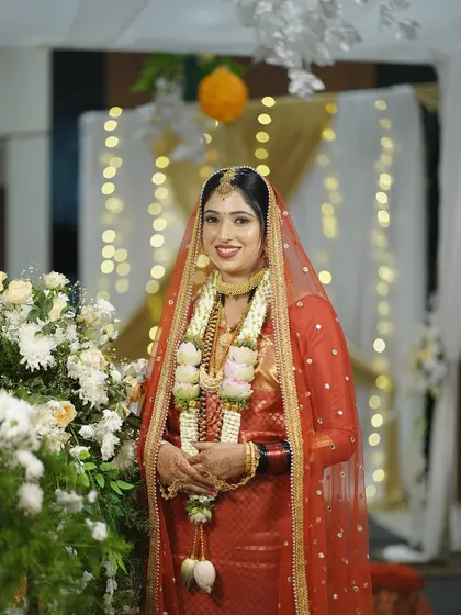 The bride posing by the floral decorations. Her makeup is flawless, and she looks happy and confident on her big day.