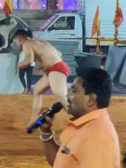 The announcer calls the play by play as two wrestlers grapple in the mud pit.