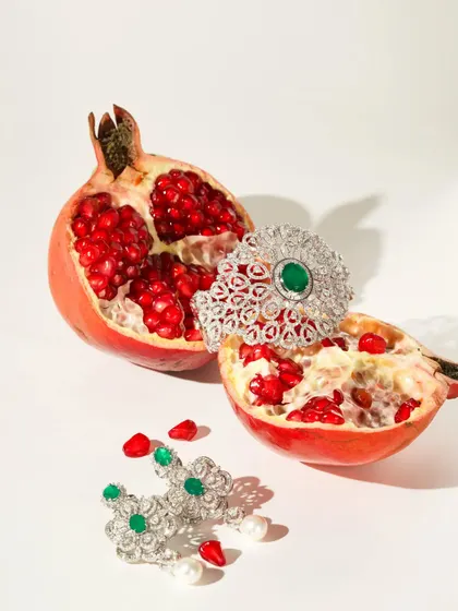 A creative and bold shot combining fine jewelry with a fresh pomegranate. The vibrant red of the fruit contrasts with the sparkling diamonds and emeralds, creating a unique and memorable image.