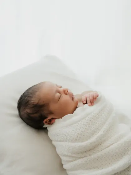 A simple and pure newborn portrait. The baby is swaddled in a white knit blanket on a clean, white background, focusing entirely on their peaceful sleep.