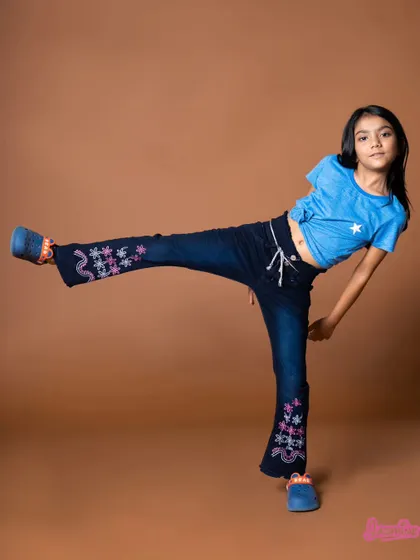 A dynamic kicking pose from a girls' fashion shoot. This highlights the flexibility and style of the jeans, perfect for an active child.