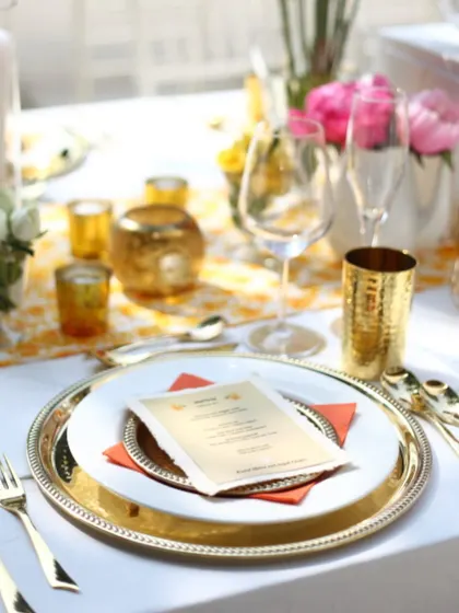 A close-up of a vibrant, sunlit table setting with gold cutlery and a custom menu. This is perfect for a celebratory brunch or lunch, where the decor feels fresh, cheerful, and elegant.