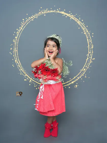 A girl in a flower dress looks surprised and happy, surrounded by a sparkling light effect. This photo has a magical and celebratory feel.