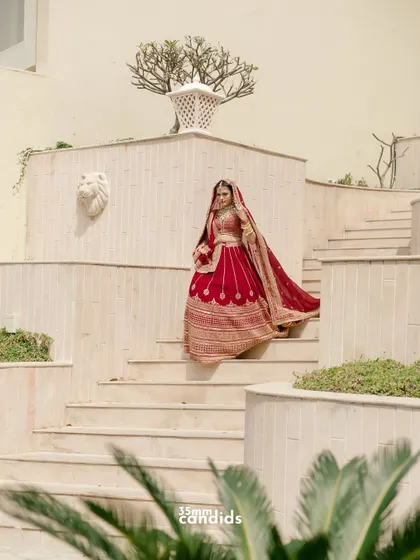 A breathtaking bridal portrait as she descends a grand staircase, her red lehenga flowing beautifully. A shot that captures the royalty and grace of the bride.