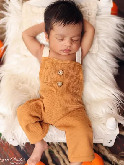 A relaxed, overhead shot of the baby boy in his waffle-knit overalls, looking peaceful on a soft fur blanket.