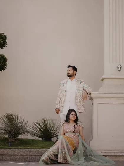 An elegant and poised portrait. The couple is posed against a grand pillar, creating a stately and classic image that showcases their beautiful pastel outfits.