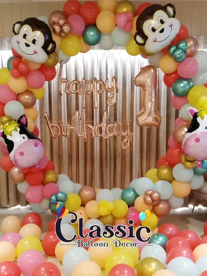 A colorful animal-themed balloon ring with monkey and cow foil balloons, perfect for a first birthday party.