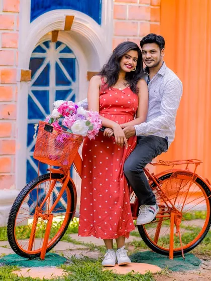 A charming portrait of a couple on a bright orange bicycle with a basket of flowers. This setup is perfect for a romantic, vintage-inspired pre-wedding photo.
