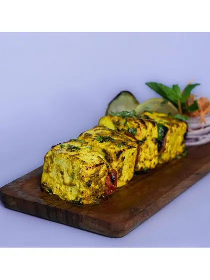 Cubes of grilled paneer tikka on a wooden board, set against a solid lavender background. The use of color helps brands create a distinct visual identity for their online presence.