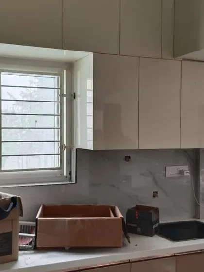 A kitchen nearing completion, with high-gloss white upper cabinets and a marble-patterned backsplash. This behind-the-scenes shot shows the project just before the final cleanup and handover.