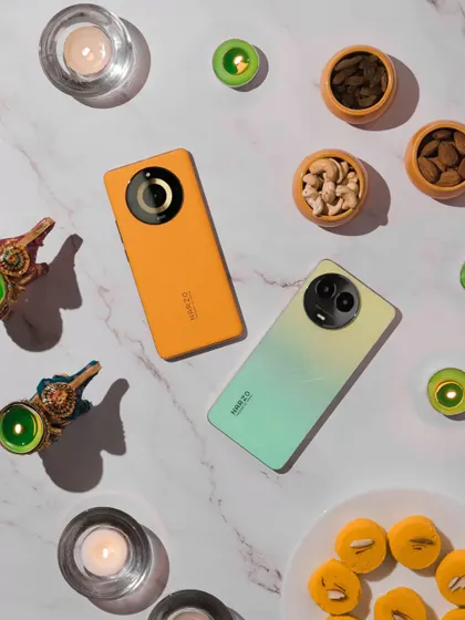 A Diwali themed flatlay with two different colored Narzo phones, dry fruits, and diyas on a marble background.