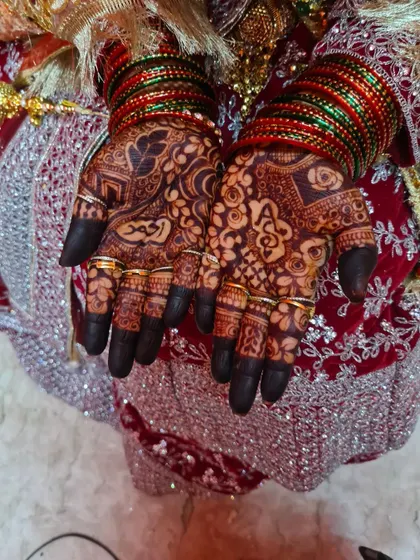 A stunningly dark stain on a bride's hands, adorned with gold rings. The personalized names 'Ahmed' and 'Ayesha' are clearly visible.