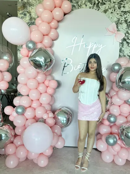 A full view of the pink and silver birthday setup, showing how the balloon garland asymmetrically frames the backdrop, creating a dynamic and modern photo corner.