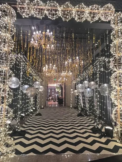An enchanting entrance tunnel for a Sangeet or reception. The design uses arches made of light-up globes, a ceiling of hanging golden tassels and chandeliers, and a bold patterned floor to create a grand welcome.