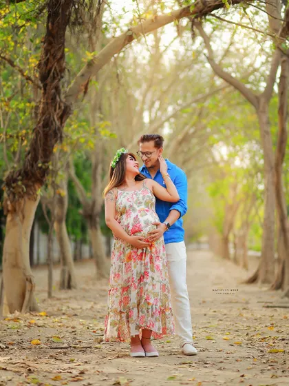 A beautiful full-length portrait of a couple on a tree-lined path. The floral dress and floral crown add a touch of bohemian charm to the outdoor setting.