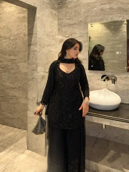 A side profile in the black suit, highlighting the sheer dupatta and neckline.