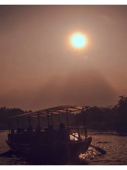 Another view of the boat tour at sunset, this time with the sun high in the sky, creating a hazy, warm atmosphere.