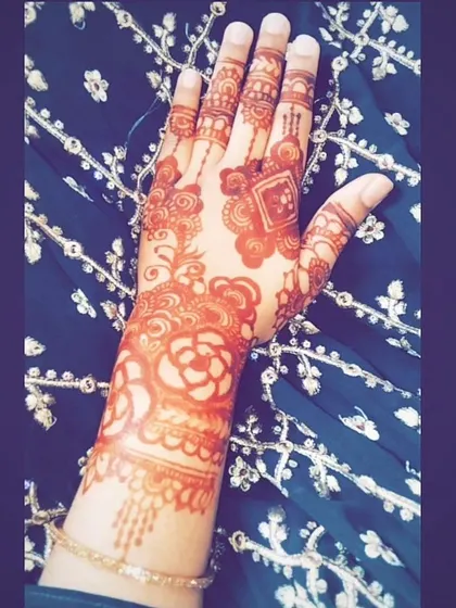 A lovely, warm henna stain against a traditional embroidered fabric. This design features a mix of rose motifs and Indian-style patterns on the fingers.