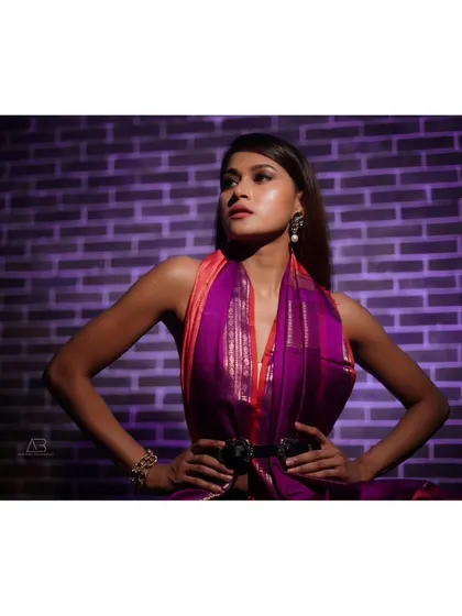 A powerful and dramatic portrait using a single light source against a purple brick wall. This shot highlights the modern styling of the saree and the model's strong presence.