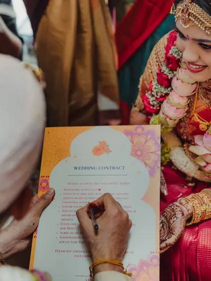 A close-up of the groom signing the playful wedding contract, with the bride looking on with a smile. It's a fun ritual that makes for great, memorable photos.