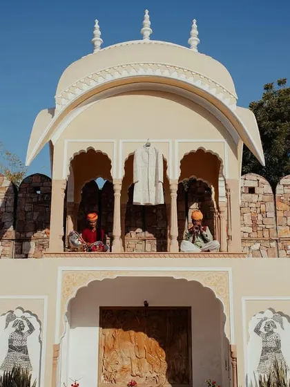 A creative shot of the groom's sherwani hanging in a royal alcove, with musicians adding to the ambiance at Nahargarh, Ranthambore.