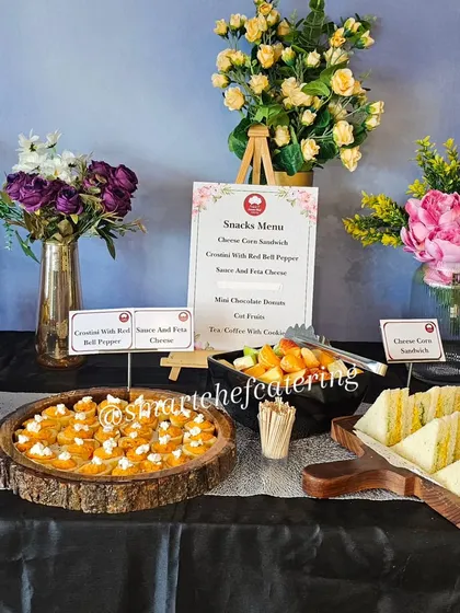 A beautiful hi-tea setup for a corporate inauguration, featuring a variety of snacks like crostini, sandwiches, and fresh fruit, elegantly displayed with floral arrangements.