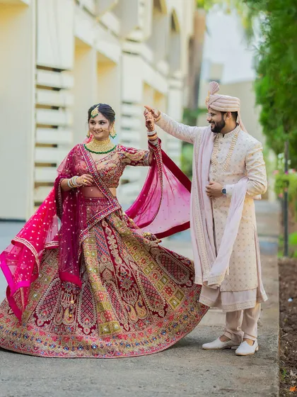 A full-length shot of the groom twirling his bride, showcasing the magnificent embroidery and flow of her red wedding lehenga.