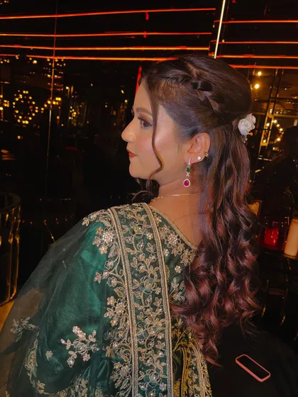 A profile shot that clearly shows the braided detail and soft curls of the hairstyle. The small flower accessory adds a delicate and feminine touch to the overall look.