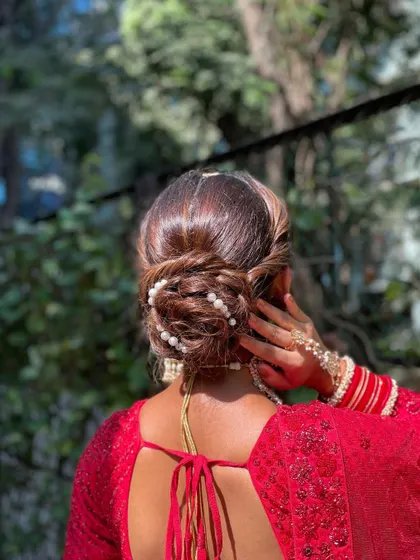 A modern take on the bridal bun, this textured updo is accented with scattered pearls. It’s a chic and sophisticated hairstyle for a bride in a contemporary red lehenga.