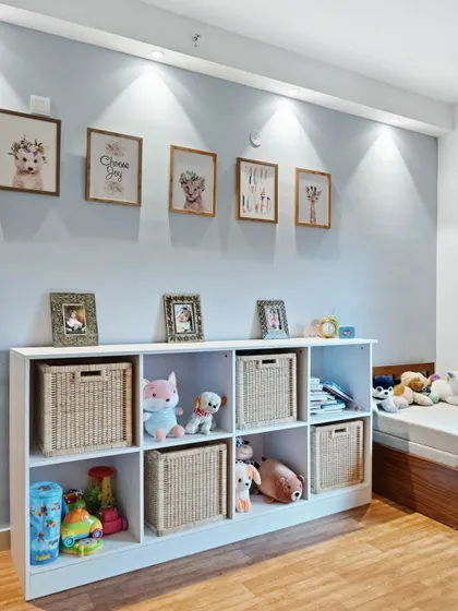 A storage solution for a kid's room, with a white shelving unit filled with woven baskets and stuffed animals. The gallery wall above adds a personal and artistic touch.